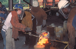 Student working with master sculpture pouring metal 
into cast