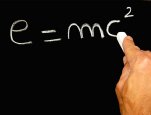 Image of a hand writing E=mc2 on a chalk board