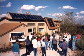 A photo of a crowd gathered near a home with solar panels on its roof.