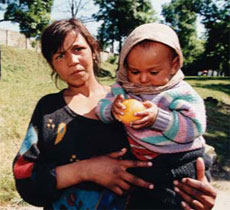 Photo of a woman holding a young infant, who has an orange in its hands.