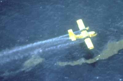 an airplane applies dispersant to a streamer of oil