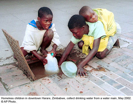 Homeless children in downtown Harare, Zimbabwe, collect drinking water from a water main; May 2002.