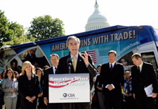 Gutierrez speaks to audience outdoors with tour bus and U.S. Capitol dome in background. Click for larger image.
