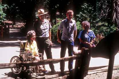 Woman in wheelchair with ranger and other visitors viewing a sign on an accessible trail