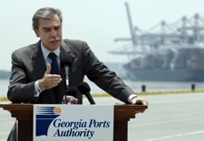Gutierrez speaking at Port of Savannah with large ship and cranes in background. Click for larger image.