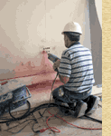 color photo of worker drilling through a plain wall