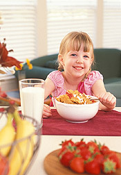 Girl eating breakfast of cereal, milk and fruit. Link to photo information