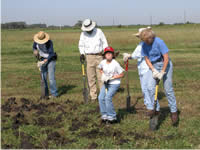 two men, two women, and a child digging holes in an open area.