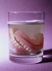 Fotografía de una dentadura postiza en un vaso de líquido