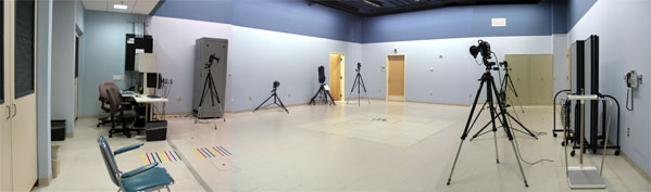 Panoramic view of the Clinical Movement Analysis Lab.  Six tripod-mounted cameras are positioned around the center area of the lab. The main Data Collection Computer and supplemental rack of equipment is positioned to the left.