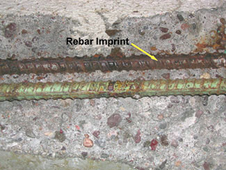 This photo shows a poorly performing ECR deteriorating in a concrete slab (a straight, top mat ECR specimen). The concrete interface above the ECR sample is completely covered with corrosion product. The ECR is separated from the concrete, and the green rebar is mottled with rust and discolored spots.