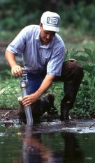 A biologist from the ARS National Sedimentation Laboratory takes a sediment core sample from the shallow margin of a stream.