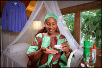 Foto: mujer sentada frente a un mosquitero, tomándose una medicina; asegúrese de tomar los medicamentos contra el paludismo en su totalidad y a las horas indicadas.