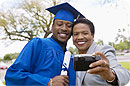 A mother and her son taking pictures of themselves; her son is in a blue graduation cap and gown holding a diploma.