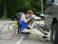 Photo of a young man on a handcycle, checking his gear.