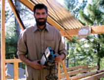 Mohammed Ayaz of the village of Malot in Bagh District received $1,000 worth of tools, including this electric planer, to help him restart his carpentry business. He is constructing the shelter behind him for a widow who cannot build for herself. 