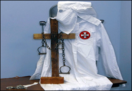 A few of the items in the Traveling Trunk, including a KKK robe, a charred cross, shackles, and a brick.