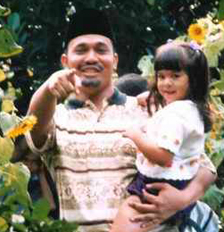 Photo of a father holding a young girl in his arms and pointing at the camera.