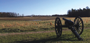 A blue sky hangs over the battlefield at Malvern Hill with a black cannon in the foreground.