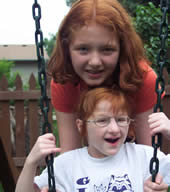 two redheaded girls smiling and playing on a swing