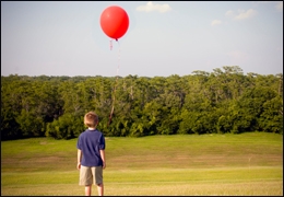 Picture of boy standing in a field with a red balloon