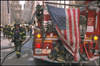 Photo of fire truck with American flag hanging over back of it and fire fighter walking on the side.
