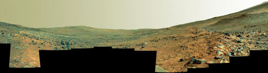 This panorama shows two rock-strewn slopes on the left and right sides of a broad, U-shaped dip in the middle.
