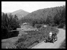 A person driving an old-fashioned car on a curving road.