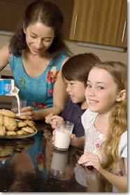 Woman with children, having milk and cookies.