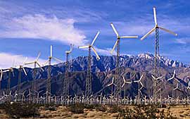 Photo: numerous wind turbines with mountain range in the background.