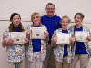 Four girls stand with their teacher and hold their award certificates