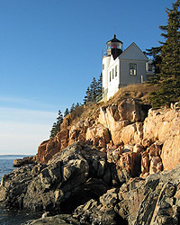 A white lighthouse sits high on a cliff over the ocean.