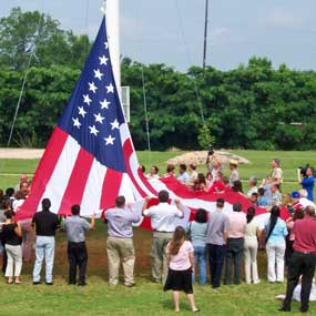 large American flag being raised on flag pole by large number of people