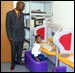 [Photo: A man stands over a child seated at a computer desk]