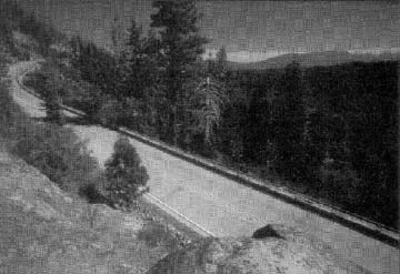 photo: hill on the left, two lane road, trees and mountains on the right