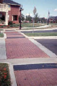 Case Study: Two different photo views of a new roundabout showing pedestrian crossings with dark grey detectable warnings and brick sidewalks.