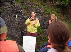 A teacher signs to students as she stands in front of a rock formation