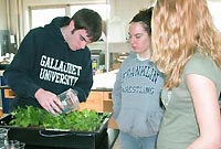 Two students look on as a student waters plants growing in a plant growth chamber