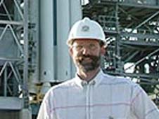 Phil Christensen stands in front of a blue and white rocket