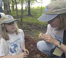 A blind, 12-year-old girl named Amelia (left) and her instructor Robin House kneeling down and touching the soil on the ground