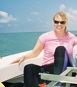 In sunglasses and a wetsuit, Heidi Dierssen sits near the edge of a boat with the ocean in the background.