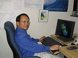 NASA scientist Lee-Lueng Fu smiles while sitting at his computer desk studying satellite images of the ocean's surface