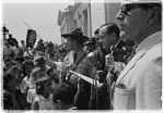 Photograph shows a group of people, one holding a Confederate flag, surrounding speakers and National Guard, protesting the admission of the "Little Rock Nine" to Central High School.
