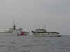 A white fishing vessel with a Coast Guard medium endurance cutter off in the distance.