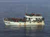 A side view small white vessel with large numbers of people on the deck and pilothouse.