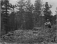 Man sits by the dump of the discovery shaft on Bramblett Lode, about 1935