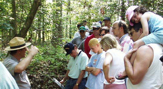 A tour of Cold Harbor.  A ranger wearing the flat hat stands to the left of a group of eight visitors of varying ages.