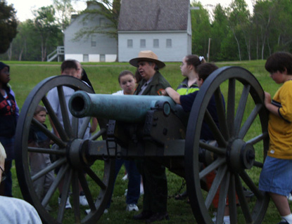 During an evening battlefield tour a ranger and middle school age children stand around a cannon.
