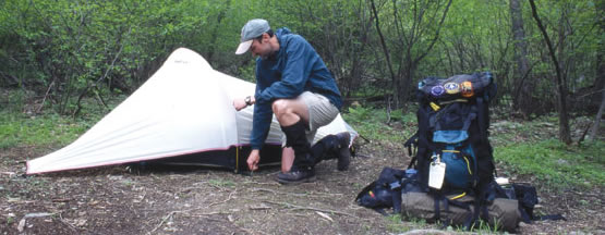A backcountry camper sets up his tent as he prepares his campsite.