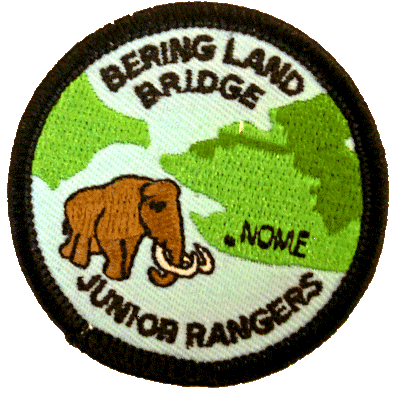 Color image of the Bering Land Bridge Junior Ranger patch, blue background, with a brown woolly mammoth and a green map of the Seward Peninsula, Alaska with Bering Land Bridge National Preserve outlined in the Seward Peninsula map.